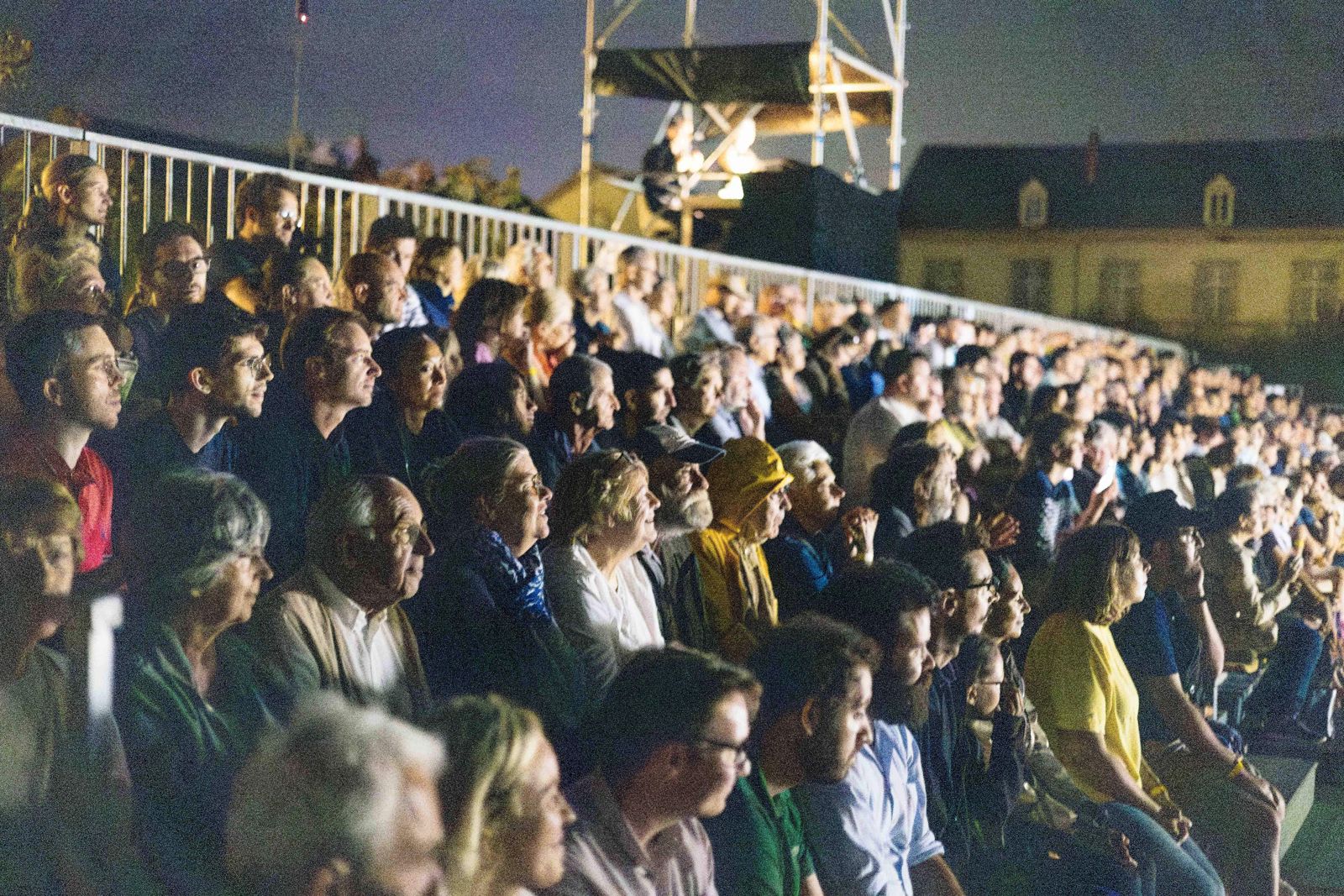 Les spectateurs des gradins regardent le spectacle, le visage éclairé par la scène